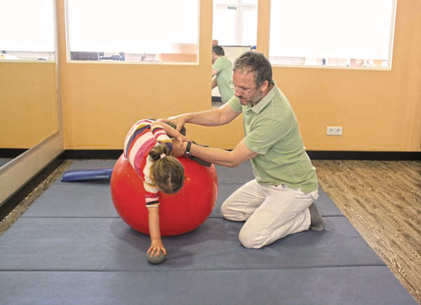 Physiotherapie Nils Hanke in einer Behandlung mit einem medzinischen Ball und einem Kind, vorwärts.